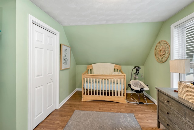 bedroom with a crib, lofted ceiling, and light hardwood / wood-style floors