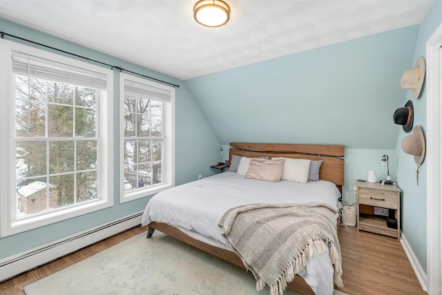 bedroom with light hardwood / wood-style floors, baseboard heating, and lofted ceiling