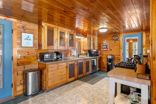 kitchen with brown cabinetry, wood ceiling, glass insert cabinets, wood walls, and a sink