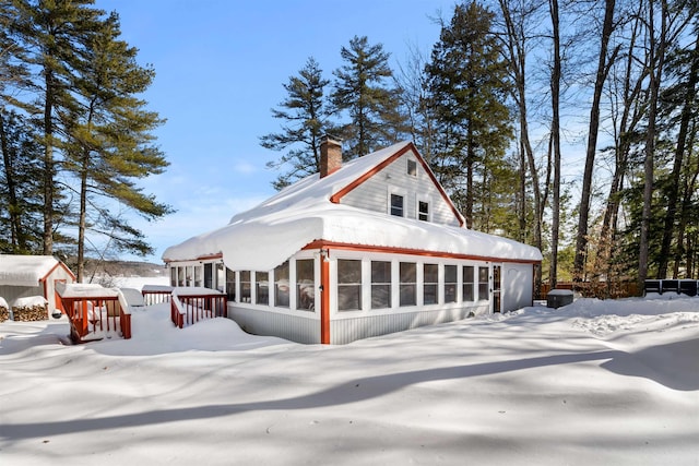 snow covered rear of property with a sunroom and a chimney