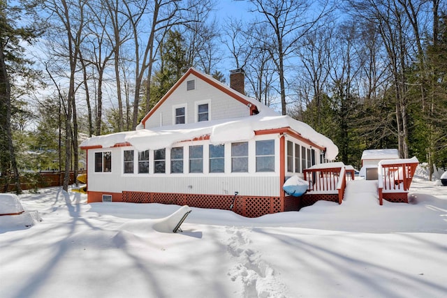 snow covered house featuring a deck and a chimney