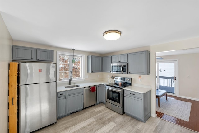 kitchen featuring appliances with stainless steel finishes, sink, light hardwood / wood-style flooring, gray cabinetry, and decorative light fixtures