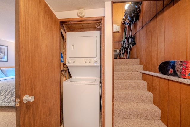 laundry room featuring stacked washer / drying machine and wooden walls