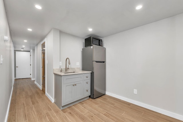 kitchen with light hardwood / wood-style flooring, light stone counters, stainless steel fridge, gray cabinets, and sink