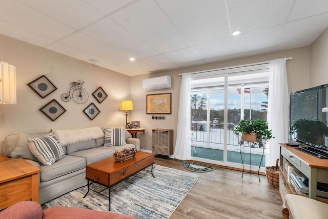 living room featuring a wall unit AC, a drop ceiling, and light hardwood / wood-style flooring