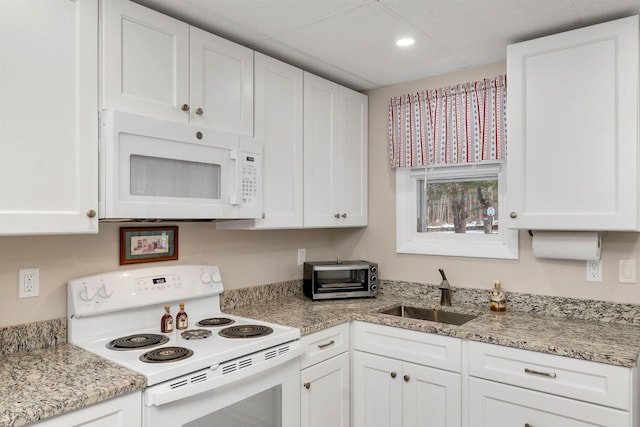 kitchen with a paneled ceiling, white appliances, light stone counters, white cabinets, and sink