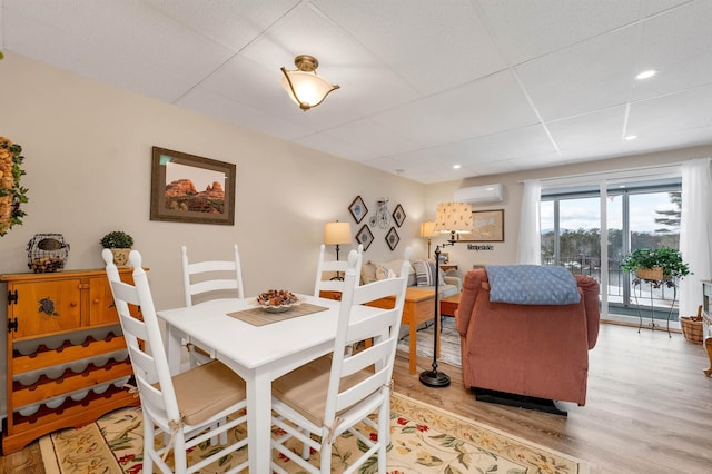 dining room featuring a wall mounted air conditioner, light wood-type flooring, and a paneled ceiling