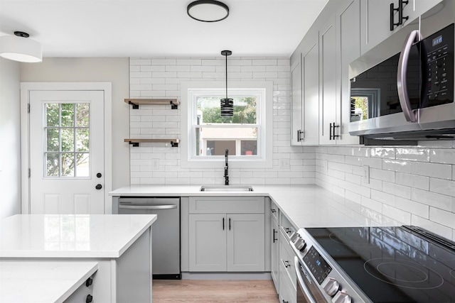 kitchen featuring appliances with stainless steel finishes, sink, gray cabinets, hanging light fixtures, and decorative backsplash