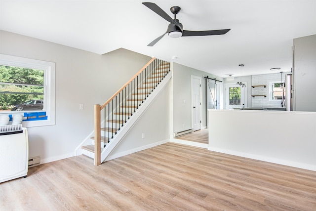 unfurnished living room featuring a baseboard radiator, ceiling fan, light hardwood / wood-style floors, and a barn door