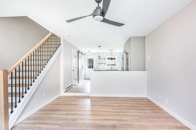 interior space with light wood-type flooring, ceiling fan, and a barn door