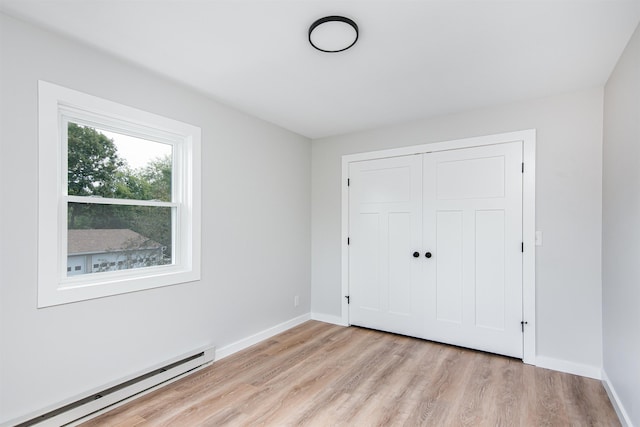 unfurnished bedroom featuring baseboard heating, light hardwood / wood-style floors, and a closet