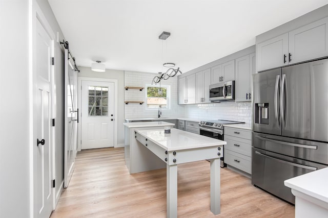 kitchen featuring light hardwood / wood-style flooring, gray cabinetry, stainless steel appliances, decorative light fixtures, and a barn door