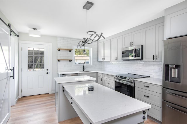 kitchen with stainless steel appliances, a center island, a barn door, sink, and pendant lighting