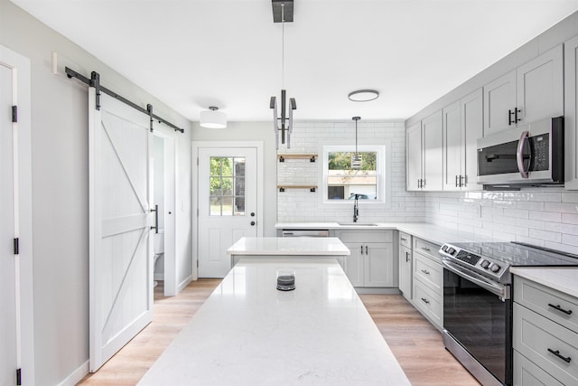 kitchen with appliances with stainless steel finishes, decorative light fixtures, gray cabinets, a barn door, and sink