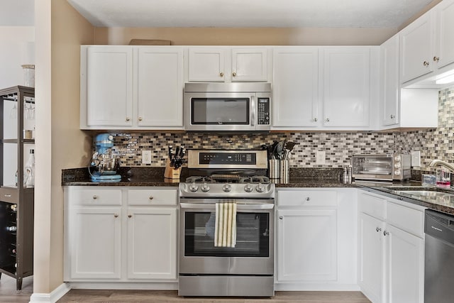 kitchen with white cabinetry, stainless steel appliances, and dark stone counters