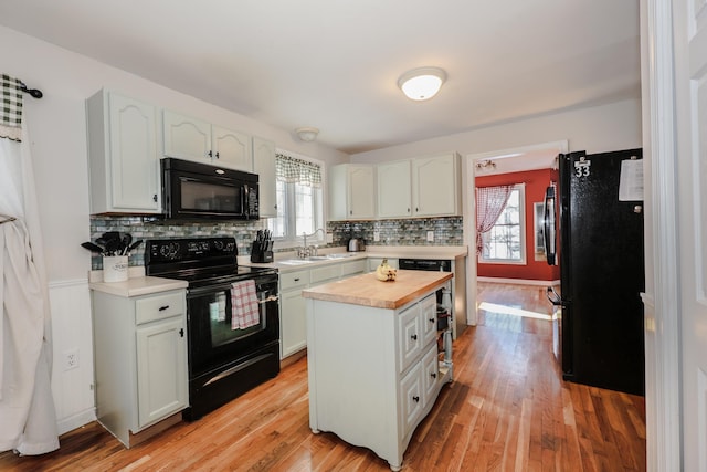 kitchen featuring plenty of natural light, white cabinets, black appliances, a center island, and sink