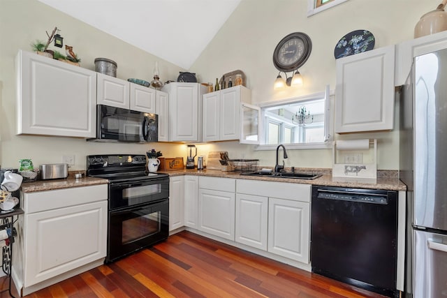 kitchen with light stone countertops, white cabinets, black appliances, lofted ceiling, and sink