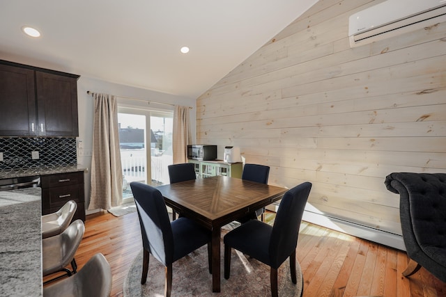 dining space with a wall mounted AC, vaulted ceiling, wood walls, and light hardwood / wood-style floors