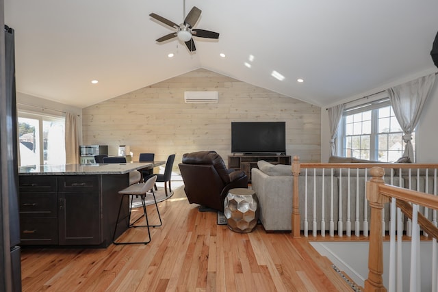 living room with an AC wall unit, light hardwood / wood-style flooring, vaulted ceiling, ceiling fan, and wooden walls