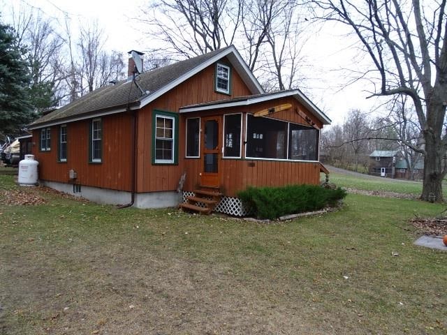 view of front of house with entry steps, a chimney, a front yard, and a sunroom