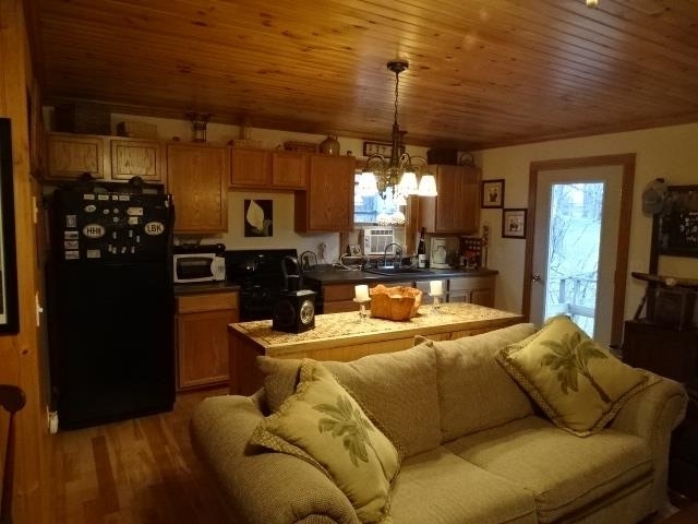 kitchen with a notable chandelier, dark countertops, stove, wood finished floors, and black fridge