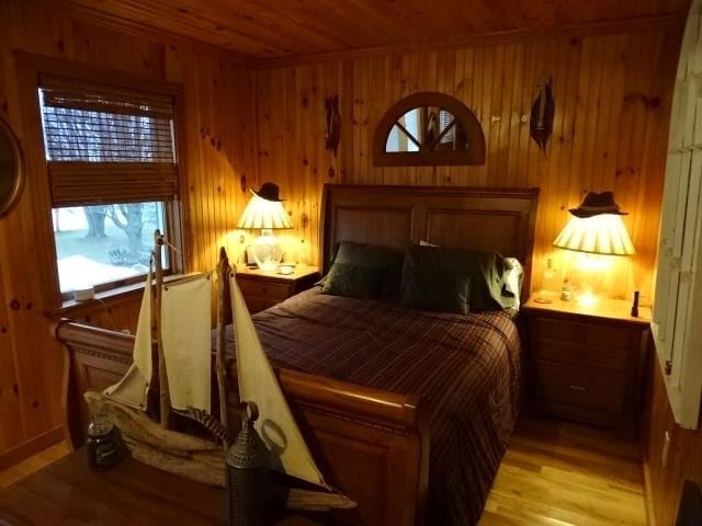 bedroom featuring wood ceiling, wood walls, light wood-style flooring, and multiple windows