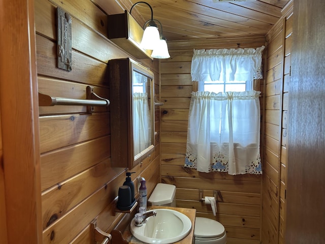 half bath featuring toilet, wood ceiling, wooden walls, and a sink