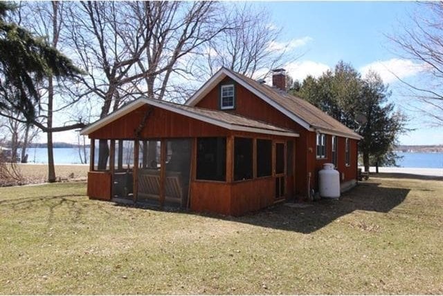 view of home's exterior featuring a water view, a sunroom, a chimney, and a lawn