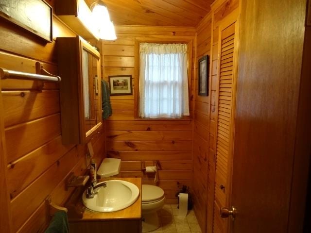 bathroom featuring toilet, wooden walls, vanity, wooden ceiling, and tile patterned floors