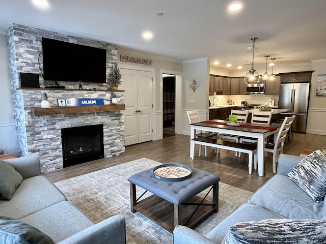 living room featuring sink, hardwood / wood-style flooring, crown molding, and a stone fireplace