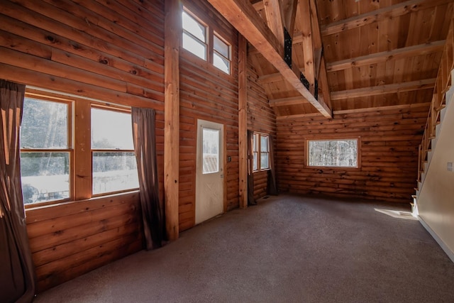 empty room with a healthy amount of sunlight, beamed ceiling, carpet floors, and log walls