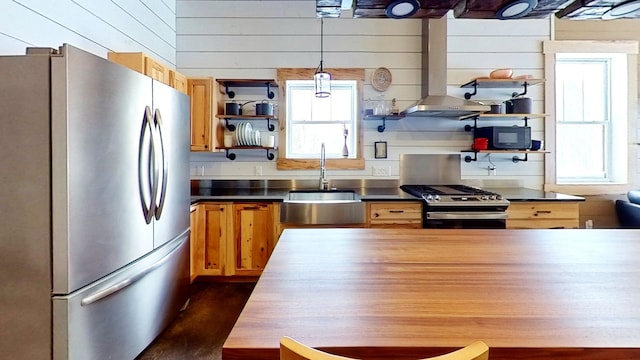 kitchen with hanging light fixtures, stainless steel appliances, wood walls, sink, and stainless steel counters