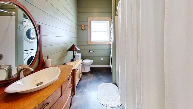 bathroom with toilet, concrete flooring, wood walls, and stacked washer and clothes dryer