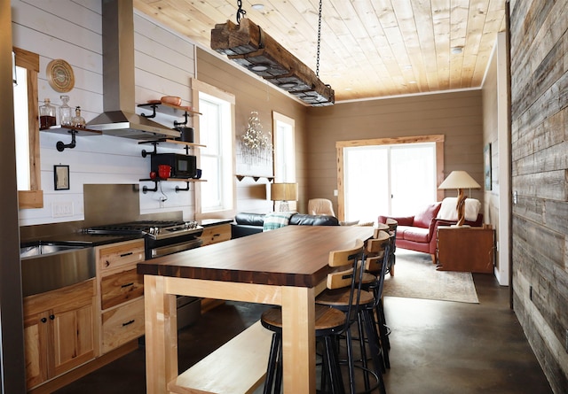 kitchen featuring wooden counters, wooden walls, wall chimney exhaust hood, wooden ceiling, and a kitchen bar