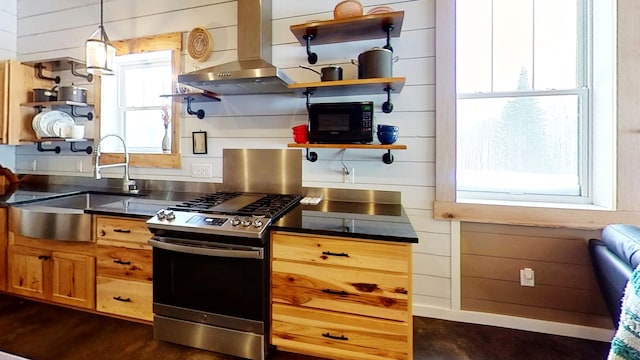 kitchen with decorative light fixtures, exhaust hood, sink, stainless steel gas stove, and wooden walls