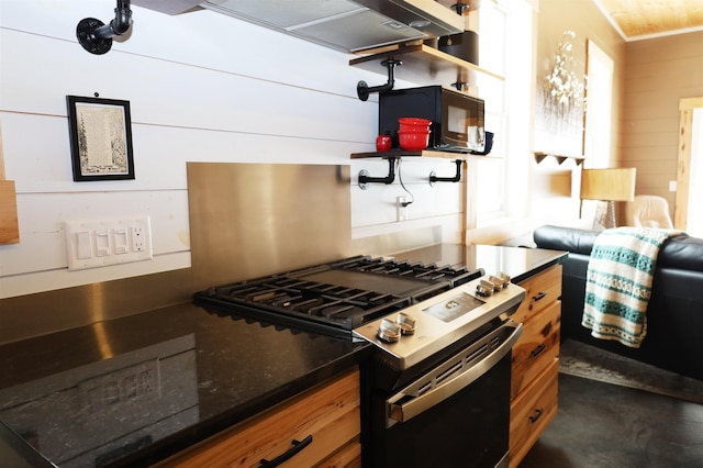 kitchen featuring dark stone countertops, wood walls, and stainless steel gas range