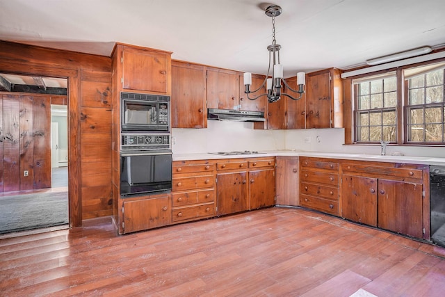 kitchen with light wood-type flooring, black appliances, an inviting chandelier, sink, and pendant lighting