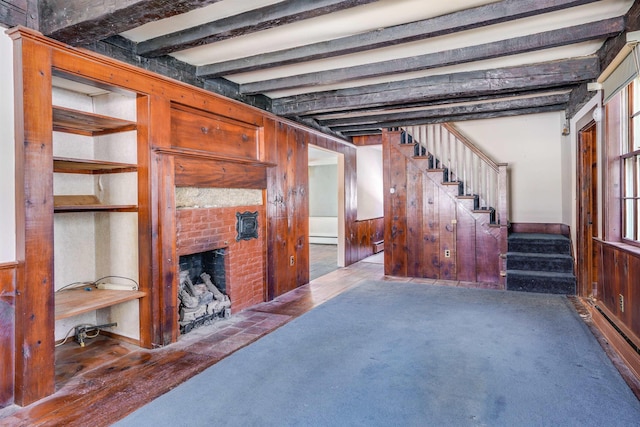 carpeted living room featuring a brick fireplace, wooden walls, a baseboard radiator, and beam ceiling