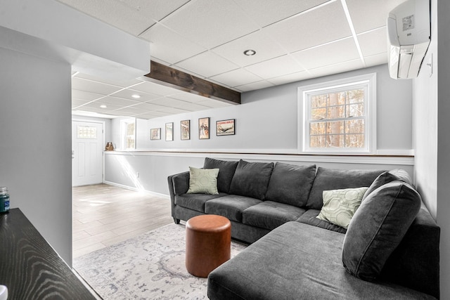 living room featuring beam ceiling, light hardwood / wood-style flooring, a wall mounted air conditioner, and a drop ceiling