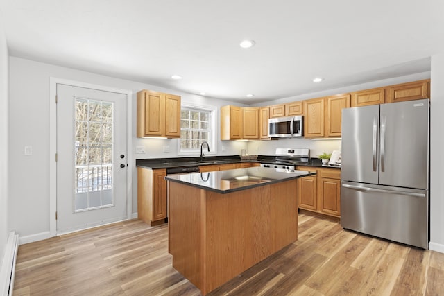 kitchen with appliances with stainless steel finishes, light wood-type flooring, baseboard heating, a kitchen island, and sink