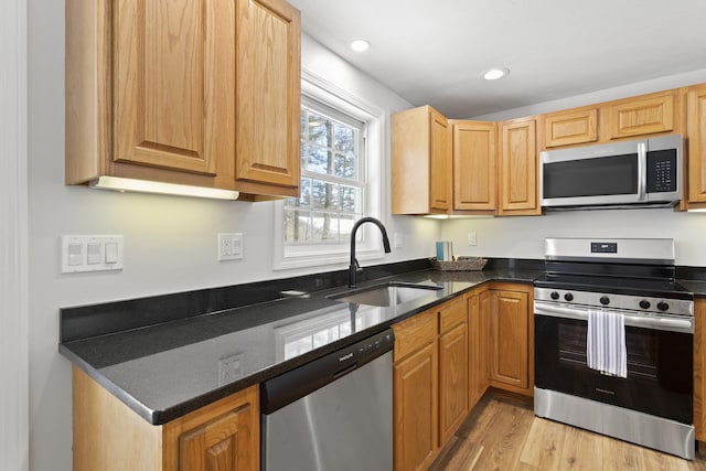 kitchen with appliances with stainless steel finishes, light hardwood / wood-style flooring, sink, and dark stone countertops