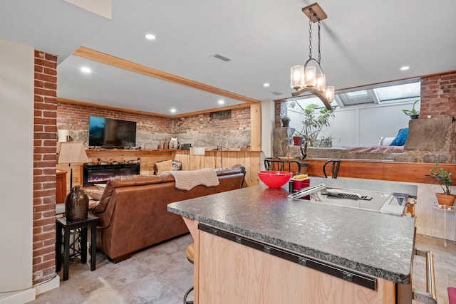 kitchen with a center island with sink, a kitchen breakfast bar, brick wall, light brown cabinets, and hanging light fixtures