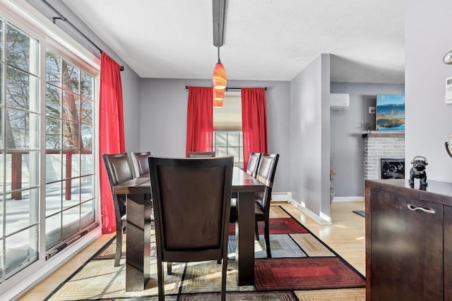 dining space featuring an AC wall unit, light hardwood / wood-style floors, plenty of natural light, and a fireplace