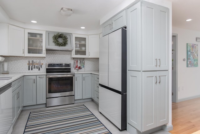 kitchen with stainless steel appliances, light countertops, gray cabinets, decorative backsplash, and glass insert cabinets