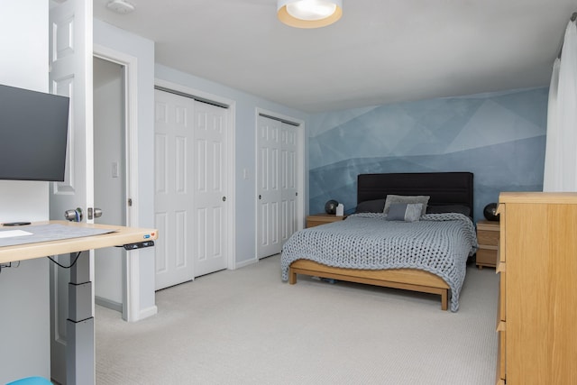 bedroom featuring baseboards, two closets, and light colored carpet