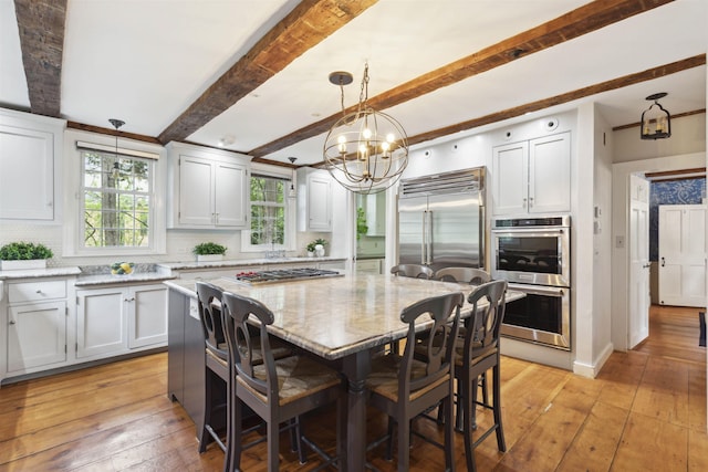 kitchen with a kitchen bar, a kitchen island, decorative light fixtures, stainless steel appliances, and light stone countertops