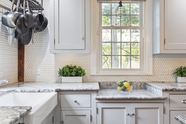 kitchen with white cabinets, sink, light stone countertops, and decorative backsplash