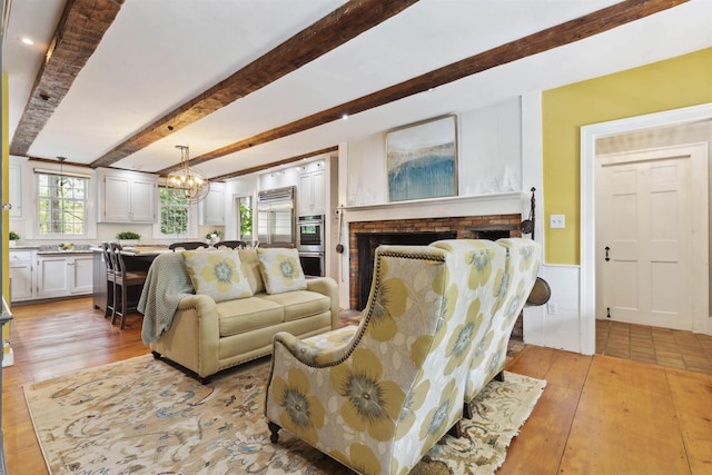 living room featuring light hardwood / wood-style floors, beamed ceiling, a notable chandelier, and a fireplace