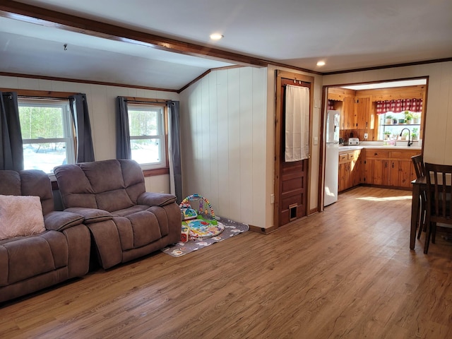 living room featuring ornamental molding, light hardwood / wood-style flooring, sink, and lofted ceiling with beams