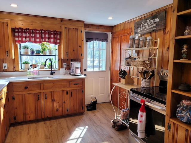 kitchen featuring sink, stainless steel electric range, wooden walls, and light wood-type flooring